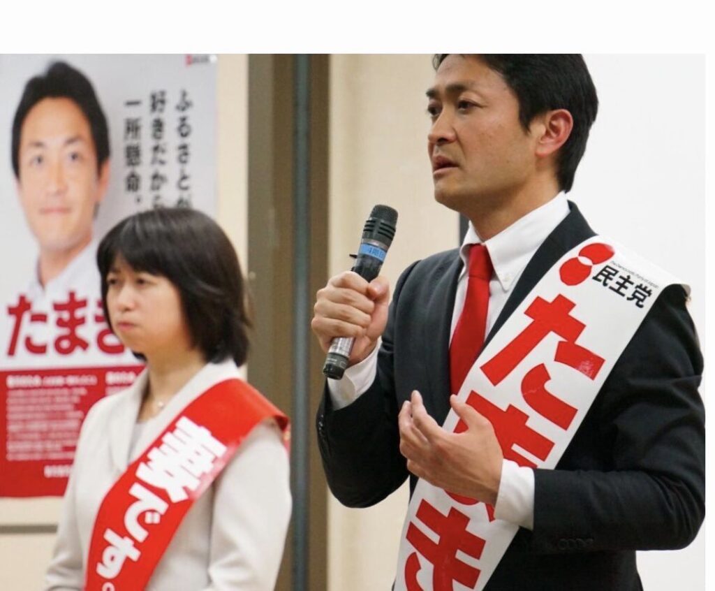 玉木恵理が「妻です」のタスキをかけて挨拶している姿